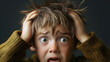 © Sunshine Design - closeup of young boy, with stress or fear, holding his head with both hands, eyes wide open, and hair tousled. Anxiety and panic on his face with dark background.