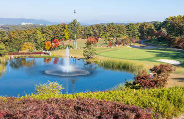 Wall Mural - Yeoju-si, Gyeonggi-do, South Korea - November 1, 2019: Fountain on a pond with autumnal golf course at Yeoju Country Club