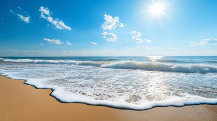 A scenic beach view with clear blue skies, the sun shining, and gentle waves lapping the shore under bright sunlight.