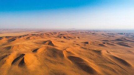 A stunning aerial view of a vast desert landscape, with rolling dunes and a clear blue sky above.