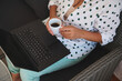 © Taras Grebinets - Woman relaxing with coffee while using a laptop on a cozy wicker chair in a casual polka dot shirt.
