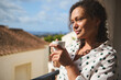 © Taras Grebinets - Woman enjoying morning coffee on a sunny balcony with a peaceful expression and curly hair in a polka dot shirt