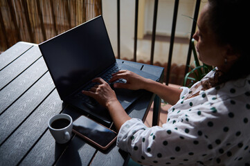 Woman working remotely on a laptop with coffee and smartphone on patio table