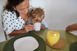© Taras Grebinets - Mother lovingly helps her child drink from a cup during breakfast at a cozy home setting