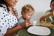 © Taras Grebinets - Mother with child enjoying morning breakfast, sharing a warm moment at the table as the toddler curiously explores a cup