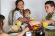 © Taras Grebinets - Family enjoying breakfast together with fresh juice and fruits at home, children reaching for grapes on a cozy morning