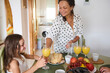 © Taras Grebinets - Smiling mother and daughter enjoying breakfast together with fresh juice and fruits in cozy kitchen setting