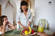 © Taras Grebinets - Mother preparing breakfast with children at home, featuring a table with fresh fruit and juice, creating a warm family morning atmosphere