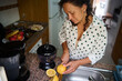 © Taras Grebinets - Woman preparing fresh lemon juice in a cozy kitchen with fruits on the counter and a juicer, showcasing a healthy and natural lifestyle.