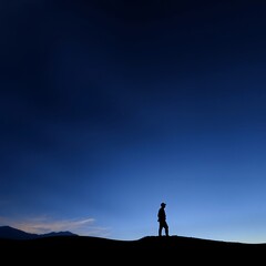 Sticker - Silhouette of a man standing on a hilltop against a twilight sky.