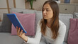 © Krakenimages.com - A beautiful young blonde woman using a tablet while sitting in her living room, with pink and gray pillows, wearing casual white clothes, in a cozy apartment setting.