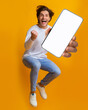 © Prostock-studio - New awesome mobile app. Jumping emotional young guy showing smartphone with blank screen on orange studio background, mockup for application or website design