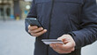 © Krakenimages.com - Young man using smartphone and holding credit card on city street, suggesting urban payment or shopping scenario.