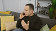 © Krakenimages.com - Hispanic man conversing on smartphone in living room, expressing with hand gesture.