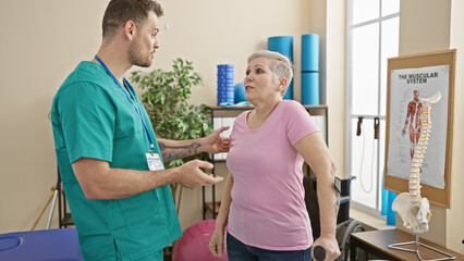 A female patient and male physiotherapist discuss treatment in a well-equipped physiotherapy clinic.