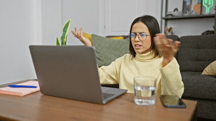 Wall Mural - Hispanic woman indoors expressing confusion at laptop in a modern living room setup.