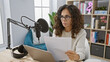 © Krakenimages.com - Hispanic woman reading script in radio studio with microphone and headphones