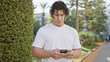 © Krakenimages.com - Handsome young hispanic man with curly hair using smartphone in city park outdoors