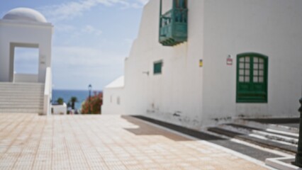 Blurred outdoor scene in lanzarote, spain, featuring defocused white buildings with green accents and bokeh background under a clear blue sky.