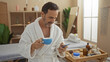 © Krakenimages.com - Mature hispanic man relaxing in a wellness spa room wearing a bathrobe and drinking from a blue cup while using a smartphone