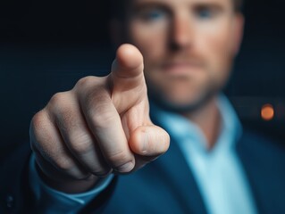 Close-up of a person in a suit pointing directly at the camera, with a focused and intense expression, set against a dark background.