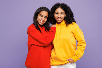 Two young cheerful fun little kid teen girls women they wear red yellow hoodie casual clothes hug put hand on shoulder look camera isolated on plain pastel light purple background. Lifestyle concept.