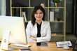 © Prathankarnpap - Attractive young businesswoman sitting at her workplace with arms crossed and smiling