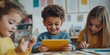 © Iryna - Three children are sitting at a table with a tablet in front of them. One of the children is smiling while using the tablet. The scene suggests that the children are engaged in a fun