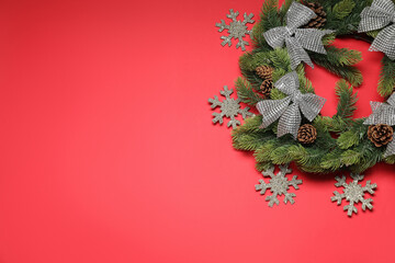 Wall Mural - Christmas wreath with snowflakes, cones and bows on red background, flat lay. Space for text