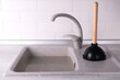 © Alsu - Clogged sink in the kitchen, plunger with wooden handle on the kitchen background, concept of removing the blockage