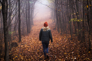 lonely woman walks on footpath in dark foggy mystery forest. spooky atmospheric mood in autumn woodl