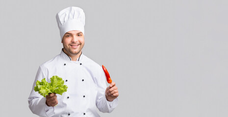 Male Chef Holding Red Pepper And Green Salad Leaves Smiling To Camera Standing Over Gray Studio Background. Panorama