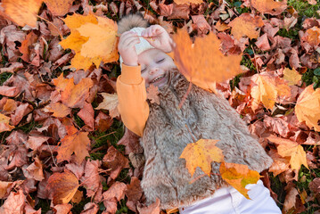 Portrait of a girl in a hat and vest lying in autumn leaves. Autumn. Emotions