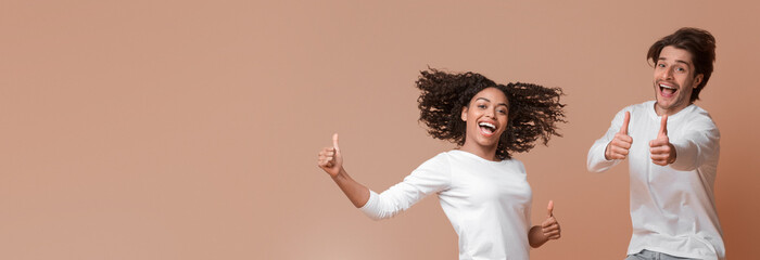 Wall Mural - Cool Offer. Excited Multiracial Couple Jumping And Gesturing Thumbs Up, Having Fun Together, Posing Over Yellow Background With Copy Space