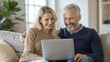 © Htet Wai Phyo - Happy middle aged couple using laptop computer relaxing on couch at home. Smiling mature man and woman talking having fun laughing with device sitting on sofa in sunny living room. Candid shot