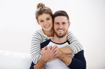 Portrait, hug and happy couple in home with support, connection and bonding together. Face, man and woman piggyback for care, healthy relationship and love for marriage on white wall in living room