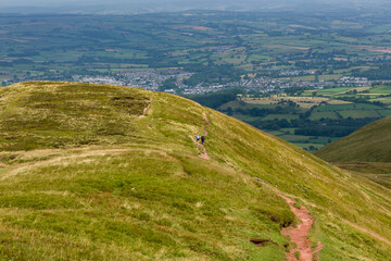 Distant hikers ascending a trail on a grass covered mountain ridge