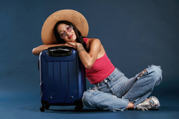 Wall Mural - Taking a rest, sitting with suitcase. Beautiful young woman is against background