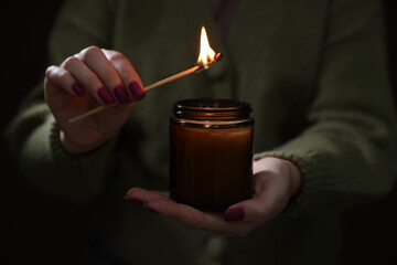 Wall Mural - Woman lighting candle with match in darkness, closeup