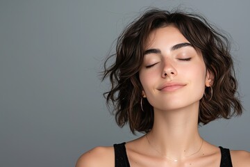 A serene woman with short curly hair enjoying a moment of relaxation, showcasing natural beauty and tranquility against a neutral backdrop.