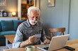 © Jelena Stanojkovic - Credit card, retirement or old man banking on laptop, internet or web for mortgage, bills or payment in home. Senior, ecommerce or elderly person for online shopping deal or investment plan research