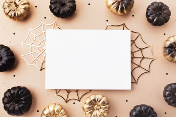 Halloween party background with paper card and fashion black and gold pumpkins with party decorations on beige table top view.