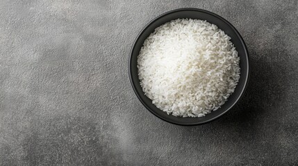 Wall Mural - Simple and elegant top view of white rice in a black bowl against a grey backdrop, focusing on the texture and detail of the rice.