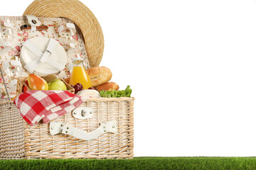 Wall Mural - Picnic wicker basket with food, tableware, bottle of juice and hat on grass against white background. Space for text