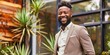 © Dougie C - Smiling African American man in a business suit standing in a modern outdoor setting with plants.