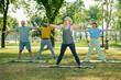 © pressmaster - Blond female fitness or yoga instructor standing in front of senior people keeping arms outstretched during outdoor training