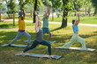 © pressmaster - Several mature active people with raised arms and outstretched legs exercising on mats on green lawn in urban environment