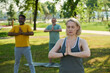 © pressmaster - Mature blond female fitness instructor showing breathe exercise while standing in front of intercultural men repeating after her