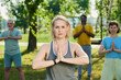 © pressmaster - Mature professional yoga instructor looking at camera while keeping her hands put together by chest during outdoor training