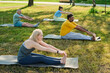© pressmaster - Side view of female fitness instructor and group of elderly intercultural men and woman doing stretching exercise on green lawn